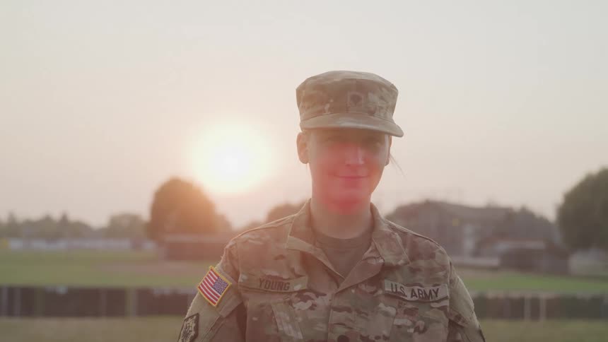 A army soldier stands in uniform facing the camera confidently during a calm sunset