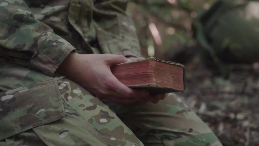 Person kneeling in a forest holding a bible