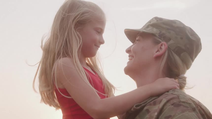 Military mother smiles after kissing her daughter on the mouth at sunset