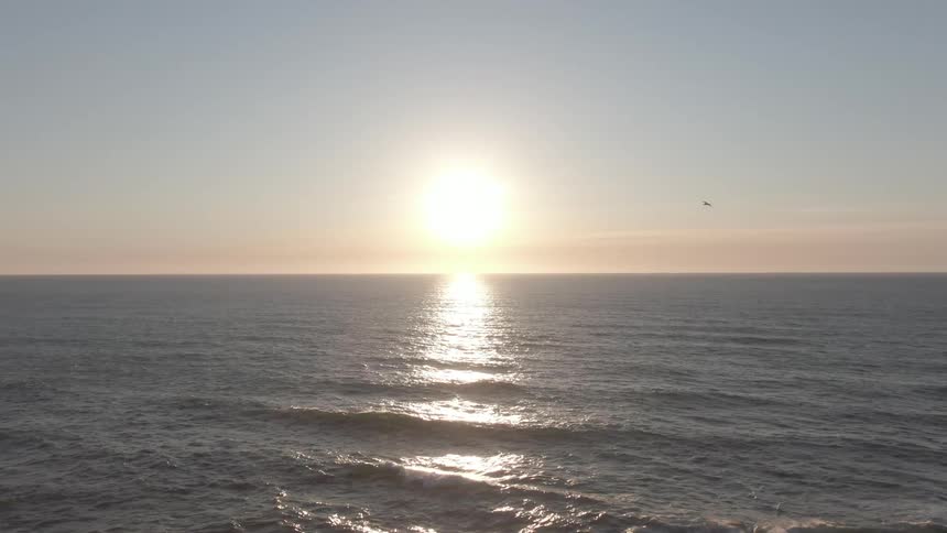The sun sets over a calm ocean casting a golden reflection across the water