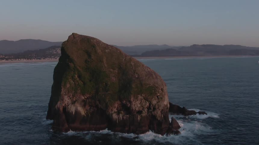 A large rock is off the shore line in the ocean