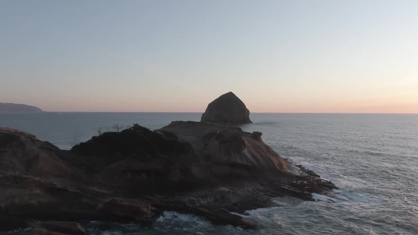 Waves splash against a promontory with a rock formation off the coast