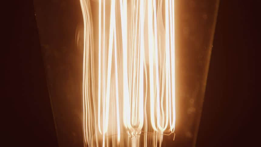 Close up of a light bulb in detail lighting up against a dark background