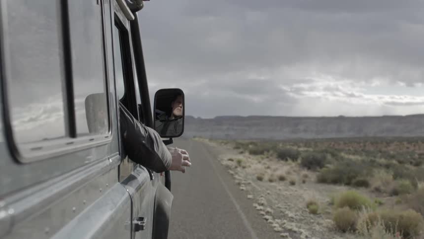 A person sticks their arm out the window as they ride in a vehicle in the desert