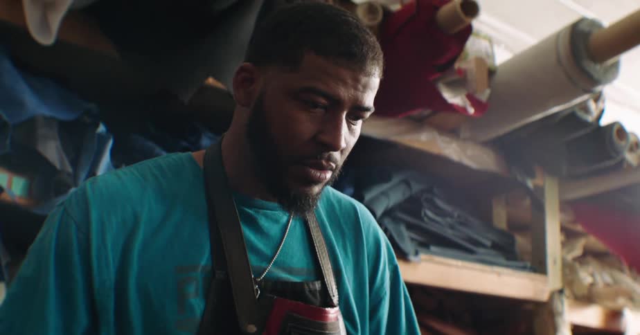 Concentrated man wearing an apron and working indoors with rolls of fabric