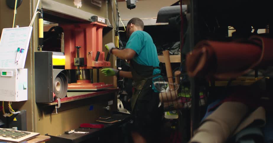 A factory worker operates a large machine in a cluttered industrial workshop