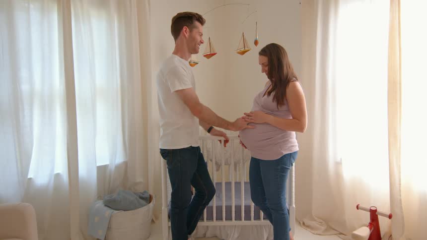 A father is touching a womans pregnant stomach as she smiles