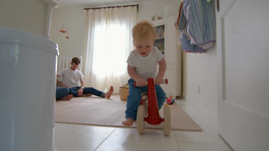 A boy rides his toy tricycle down the hall