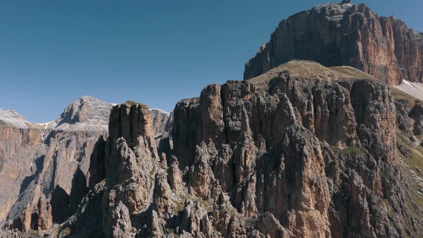 A sweeping aerial view reveals the majestic rugged peaks of the dolomite mountains under a clear blue sky