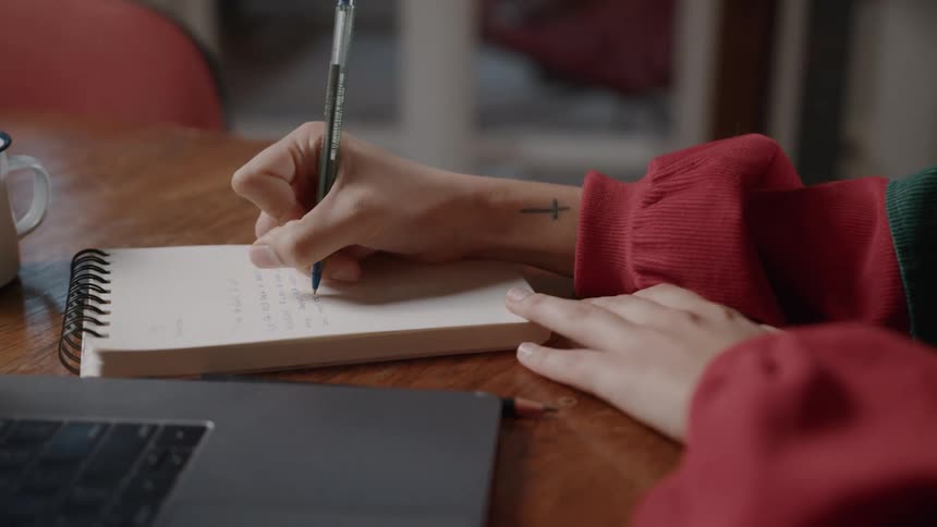 A person writes in a notebook with focus on their hand and pen