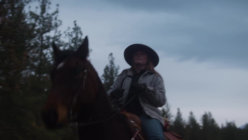 A woman is riding her hose and looking around at the trees