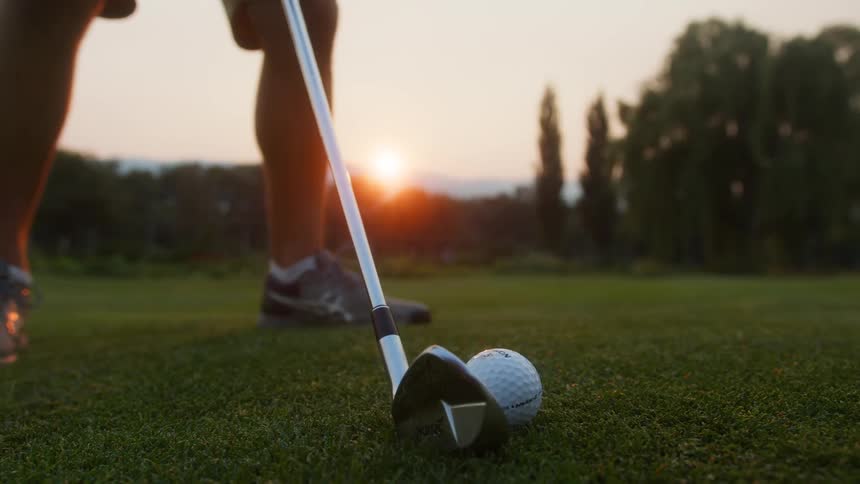 A golfer prepares to swing at a ball on the green during sunset