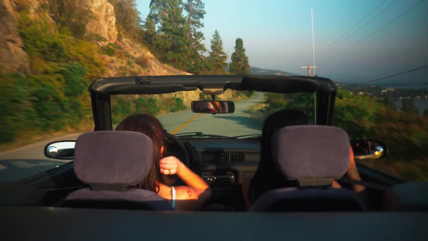 Two women in a convertible car on a road through the mountains