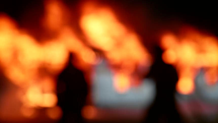 Silhouette of two human figures towards a fire disaster at night