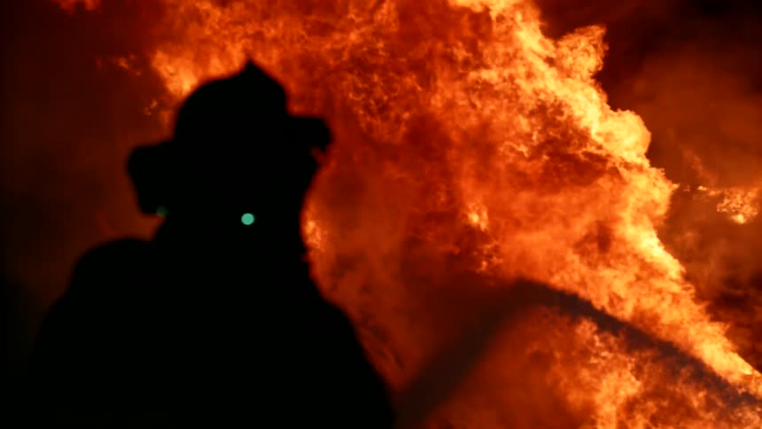 A firefighter uses a fire hose to spray water on a burning fire at nighttime