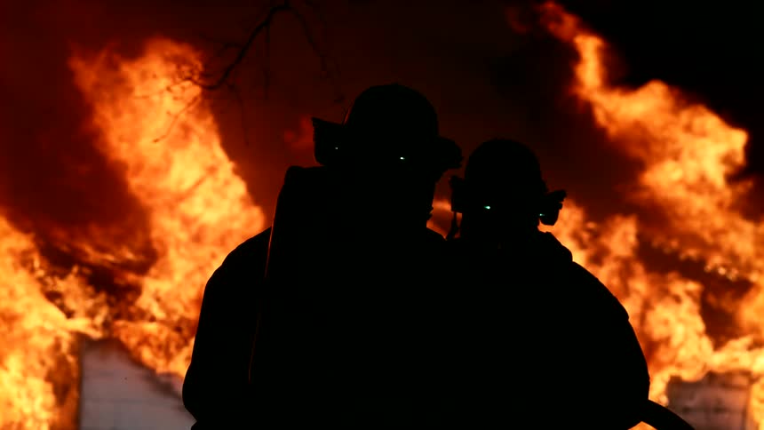 Two firefighters hold the hose while trying to put out a burning home