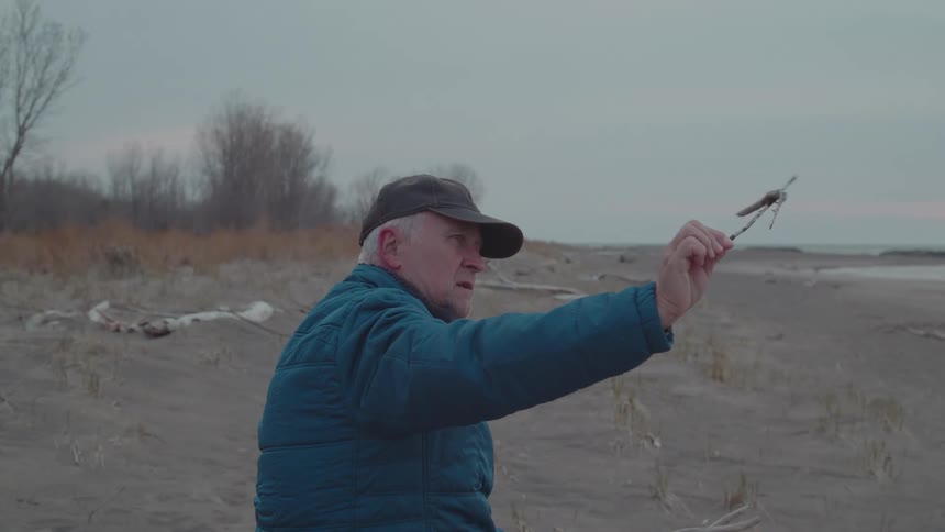 A man examines a piece of wood on the beach