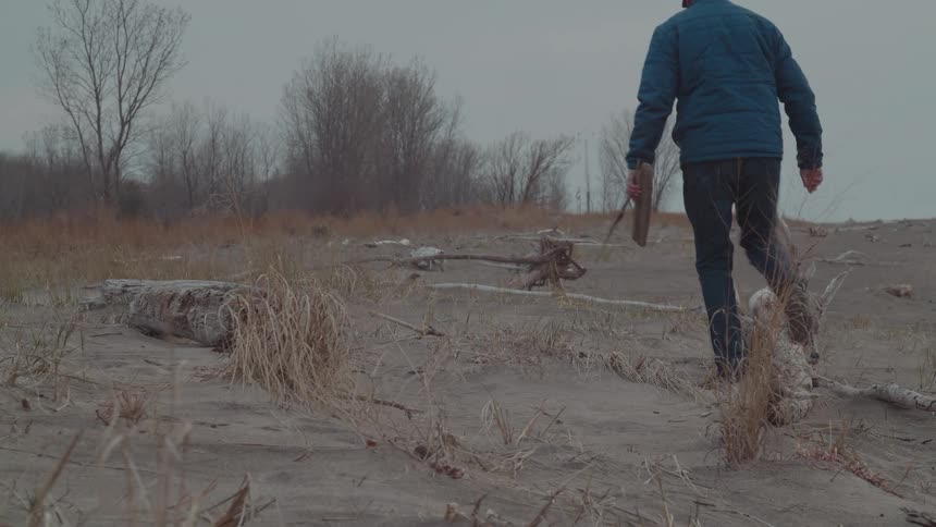 A man walks through a desolate area stepping on a large tree branch