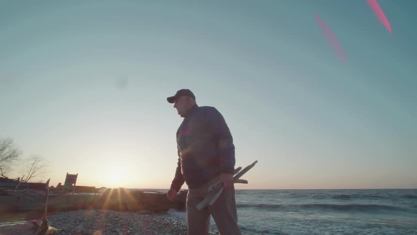 Man in cap on a beach holding branches