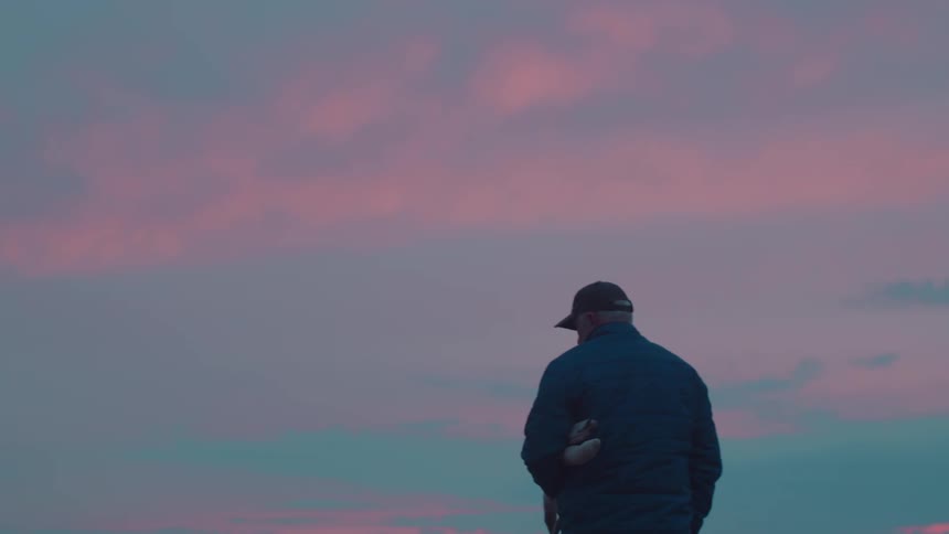 Man in cap on a purple sky sunrise walking carrying pieces of wood