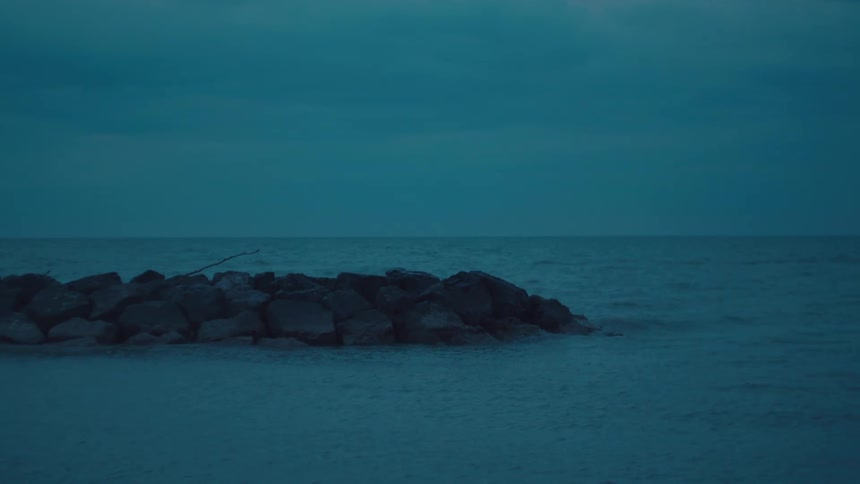 A rocky jetty extends into the calm sea under a blue evening sky