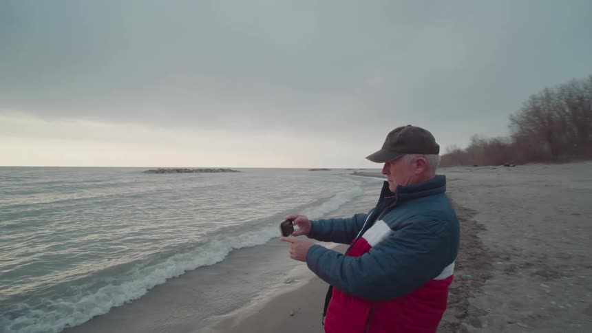 Man in a cap filming a beach with his smartphone