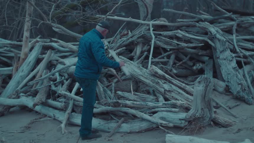 Older man gathering driftwood from a very large pile stacked on the beach