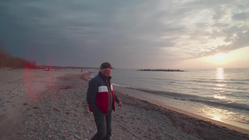 A man walks alone along a pebbled beach at sunset