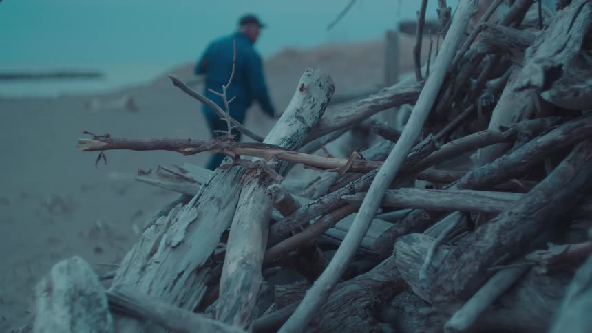 A man carries driftwood past a pile of driftwood