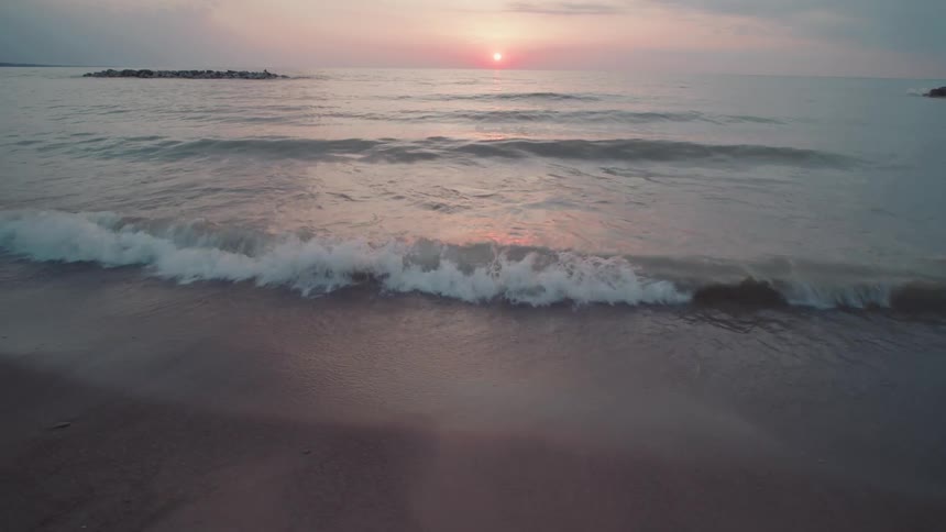 Waves roll in to shore and over the beach as the sun glows on the horizon