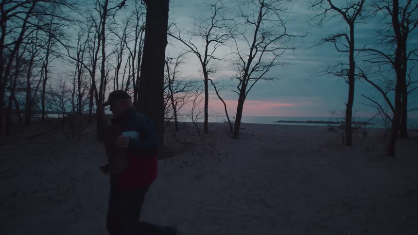 Man walking along the beach carrying a wooden branch