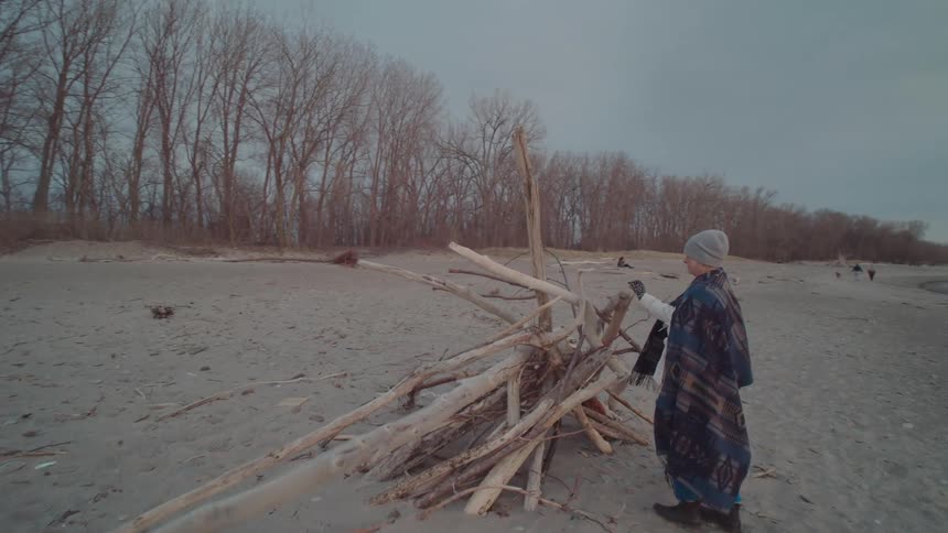 A woman walks up to a stack of driftwood on the beach