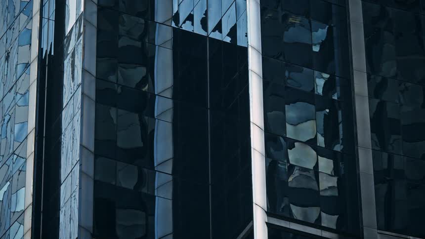 Sunlight & clouds reflect on the windows of a tall glass building