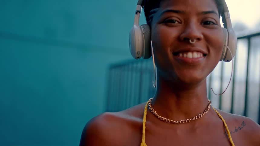 A young woman smiles while wearing headphones and looking at the camera