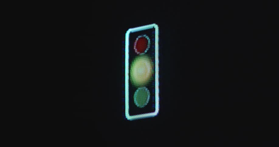 Dark and pixelated pc screen with RGB panel displaying a traffic light against a dark or black background flashing and blinking the shiny yellow light as a warning signal or symbol
