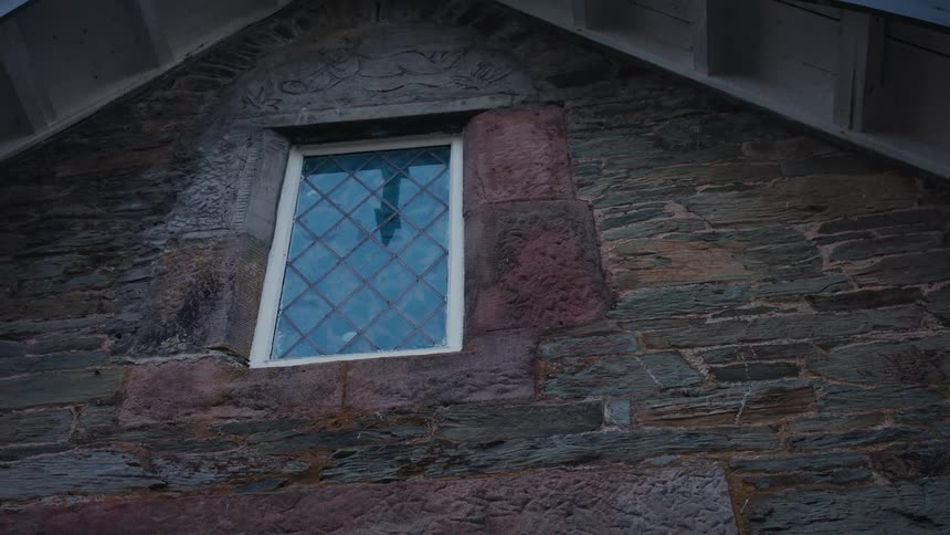 A building with a window near the roof and visible burglar bars is seen around midday