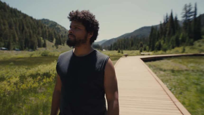 A man walks alone on a wooden path through a scenic mountain valley on a sunny day