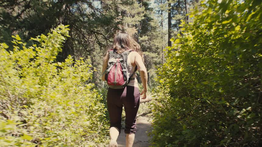 A woman runs along a forest trail with a backpack