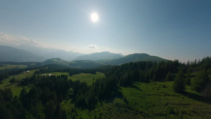 Aerial view of a sunny mountain landscape with forests and grassy hills