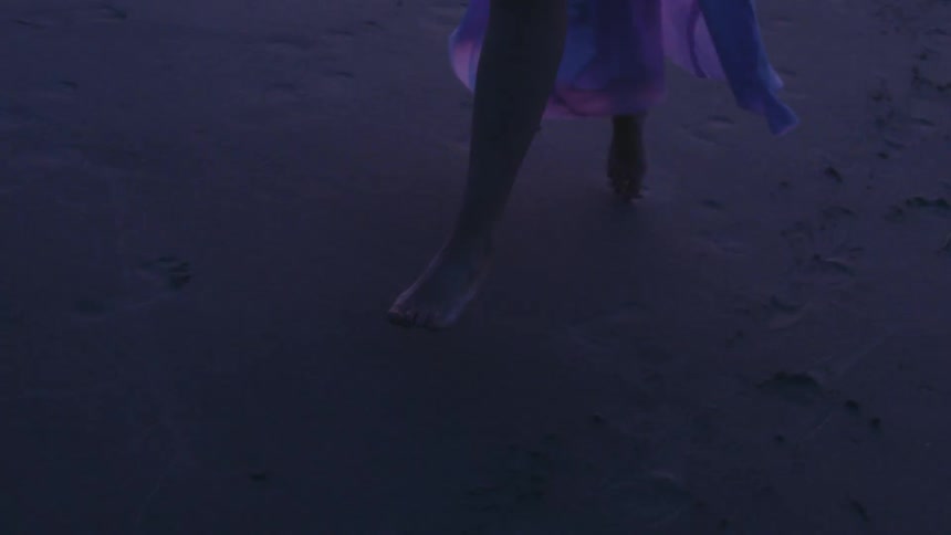 Legs of a person with bare feet and a long dress running on the sand
