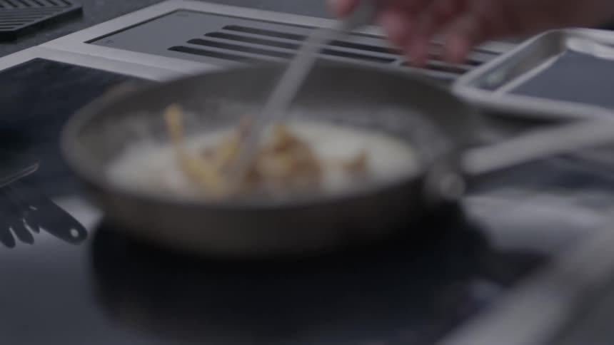 A frying pan with food sizzles on a stove in a professional kitchen