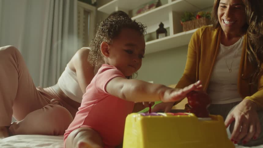 Little girl playing on the bed accompanied by two adult women