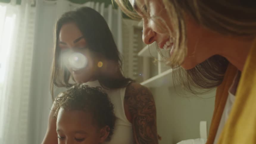 A mother plays with her child on her lap indoors while another woman sits beside them all enjoying a pleasant time with the baby