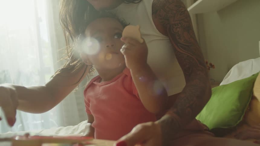 Two women play with a child on top of the bed in the bedroom around midday