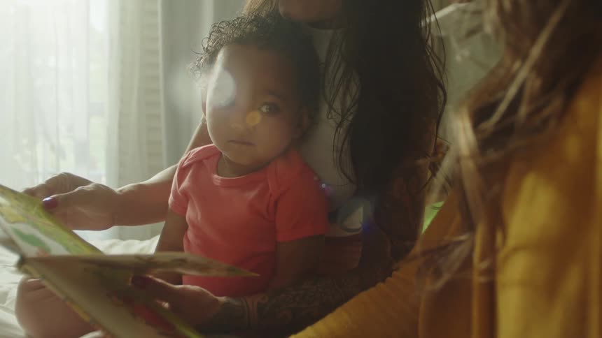 A girl sits on her moms lap while she flips through a book