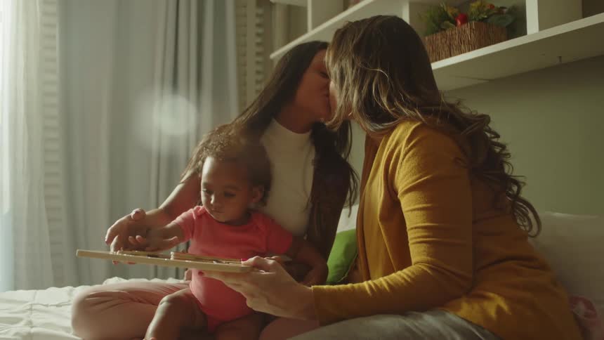 Lesbian couple kissing and caring for a small child in bed