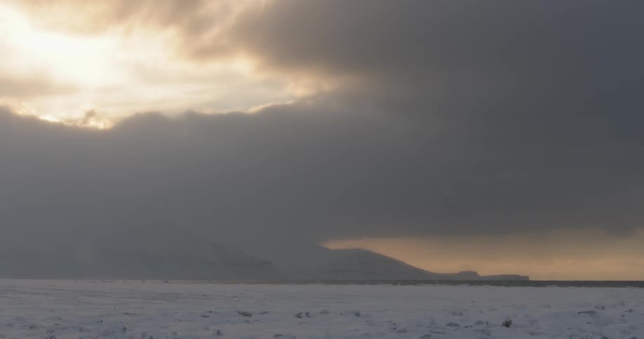 The field is covered with snow and the sky is full of clouds at dawn