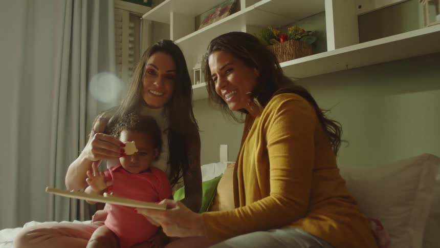 Two smiling adult women playing with a small child on the bed