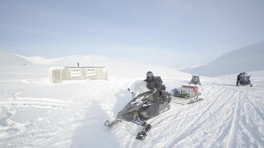 A few people riding on snowmobiles and pulling wagons behind them