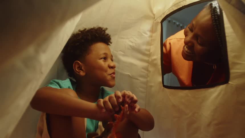 Smiling mother talking to her son who is playing inside a tent